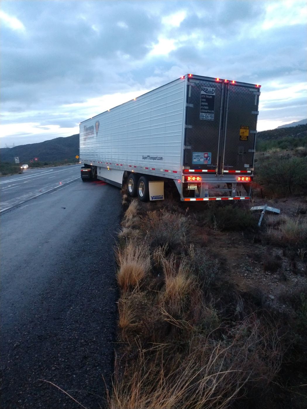 A refrigerated trailer parked on the shoulder of a highway at dusk